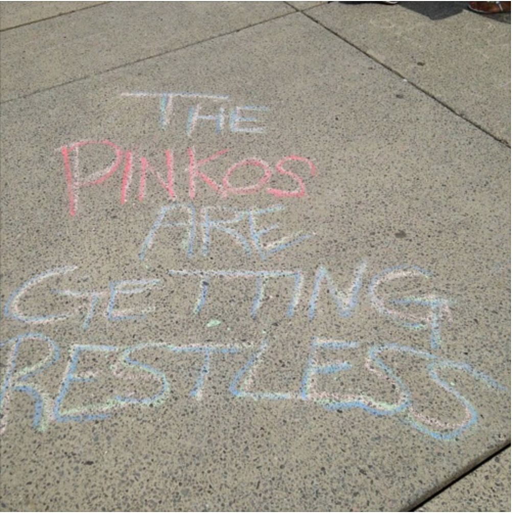 A photo of sidewalk chalk writing. It reads 'the pinkos are getting restless'.